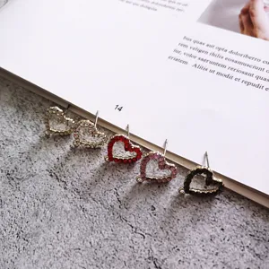Primo piano di componenti per orecchini a cuore in strass scintillanti e materiali fai da te.