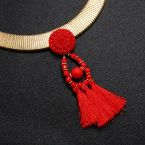 Detailansicht einer goldenen Schlangenkette mit auffälligen roten Quasten und Anhänger.
