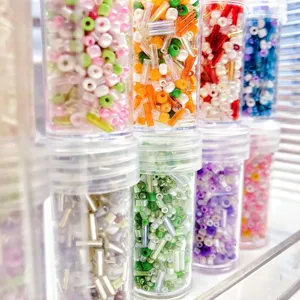 Dettaglio ravvicinato di perline colorate e tubolari in barattoli di plastica trasparenti.