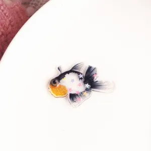 Primo piano dettagliato di un ciondolo in resina a forma di pesce rosso con stelle.
