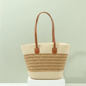 Dettaglio della borsa tote in paglia intrecciata con manici in pelle marrone per l'estate.