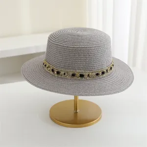 Vista detallada de un elegante sombrero de paja gris plano con cinta de diamantes de imitación.