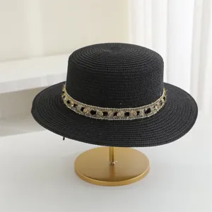 Detalle del sombrero de paja negro con banda decorativa dorada y ala plana.