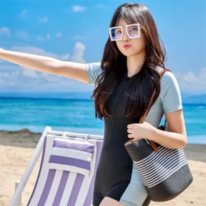 Detail view of a striped woven beach tote bag carried by a model on a sunny beach.