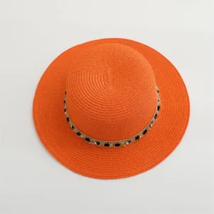 Primer plano del sombrero de paja plano naranja con elegante banda decorativa negra y dorada.