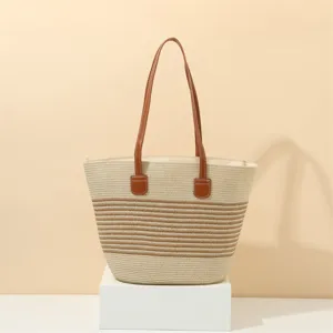 Close up of the woven straw tote bag featuring brown leather shoulder straps and striped detail.