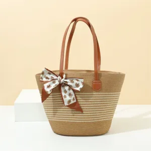 Straw tote bag detail featuring striped woven body, brown leather handles and a floral scarf.