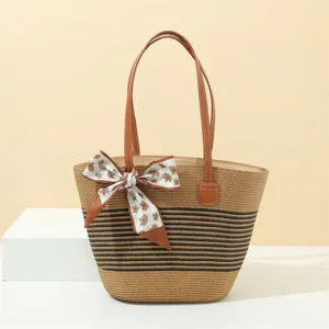 Detail view of straw tote bag with black stripes, brown leather handles and chic floral scarf.