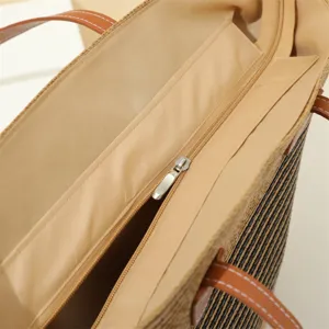 Woven straw tote bag with striped pattern, zipper closure, and brown leather straps for summer.