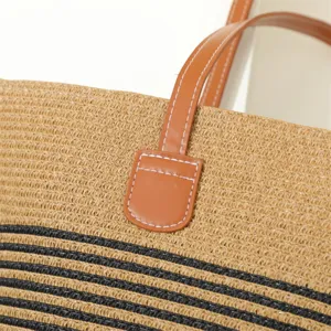 Straw bag detail view showing woven texture, brown leather handle and black stripe decoration.