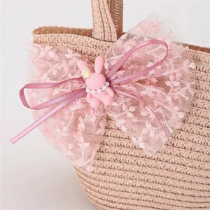 Detalle de bolso de paja rosa con lazo de encaje y tierno conejito, accesorio infantil.