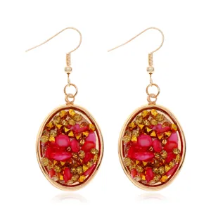 Pendientes colgantes ovalados dorados con piedras trituradas rojas y tachuelas doradas.