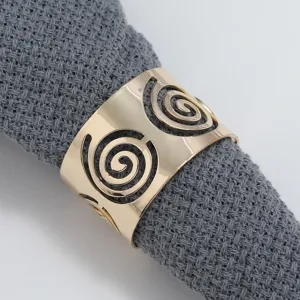 Detailed close-up shot of gold metal napkin ring with hollow spiral design on grey fabric.