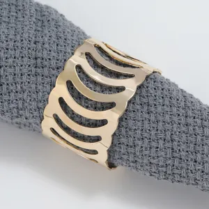 Close-up of gold metal hollow napkin ring on grey cloth fabric table setting detail.