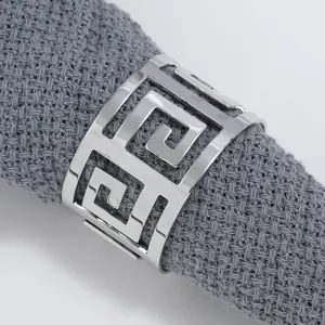 Silver metal napkin ring featuring a hollow-out Greek key geometric pattern on grey fabric.