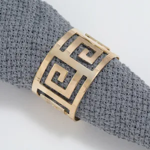 Gold metal napkin ring featuring classic Greek key hollow design holding grey cloth napkin.