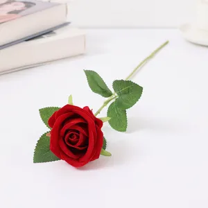 Primo piano dettagliato di una singola rosa artificiale rossa in velluto con foglie verdi per casa.