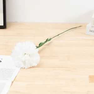 Artificial white carnation detail shot, single silk flower stem on wood table surface.