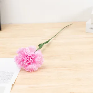 Close-up detail of artificial pink carnation flower stem, soft fabric petals and green leaves.