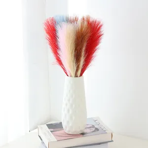 Artificial pampas grass in white vase detail shot, colorful faux reed home decor arrangement.