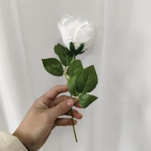 Close-up detail view of a white artificial rose flower with green leaves, indoor decor.