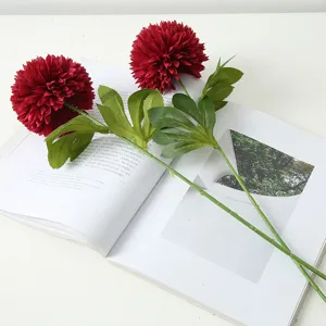 Red artificial globe chrysanthemum bouquet detail showing realistic flower head and green leaves.