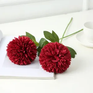 Detailed close-up shot of vibrant red artificial ball chrysanthemum silk flowers on a clean white book surface.