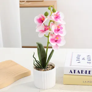 Artificial orchid potted plant with white vase and decorative stones for home room decor