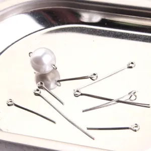 Detail view of DIY jewelry making accessories, including silver headpins and faux pearl beads.