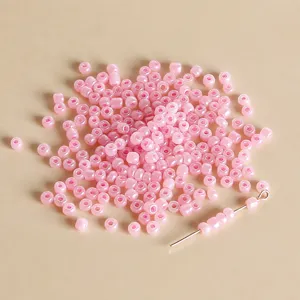 Close-up detail of 3mm pink jelly seed beads scattered with a golden beading pin for DIY jewelry.