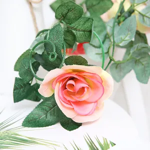 Detailed close-up view of artificial rose flower vine with pink silk blossoms and green leaves.