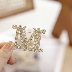Nahaufnahme der glitzernden Strass-M-Brosche, elegantes goldenes Mode-Accessoire für Damen.