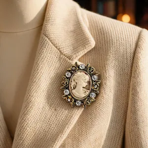 Dettaglio di spilla cammeo vintage con cristalli strass e rose metalliche su blazer beige.