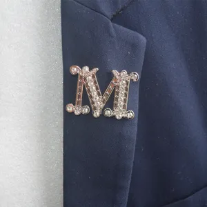 Detailansicht einer glitzernden Kristall M Buchstaben Brosche elegant auf dunklem Stoff.
