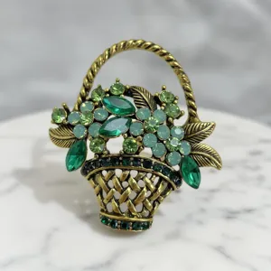 Detailed view of vintage green rhinestone basket brooch with antique brass metal and crystals.