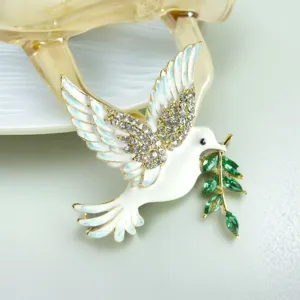 Detailed view of peace dove brooch featuring white enamel, clear rhinestones, and green crystal leaves.