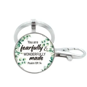 Detailopname van zilveren metalen sleutelhanger met inspirerende quote en groene bladeren.