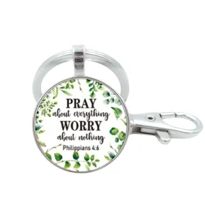 Gedetailleerd overzicht van een metalen sleutelhanger met religieuze quote en groene bladeren.