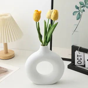 Modern white donut ceramic vase with artificial yellow tulip flowers for home decor.