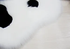 Close-up detail of soft fluffy white cat paw rug with black spots on wooden floor texture.