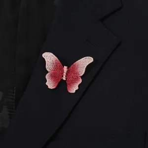 Close-up of a pink gradient embroidered butterfly brooch on a black suit lapel detail.