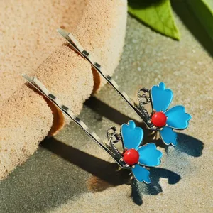 Détail d'épingle à cheveux florale en émail, avec pétales bleus et perle rouge, style ethnique.