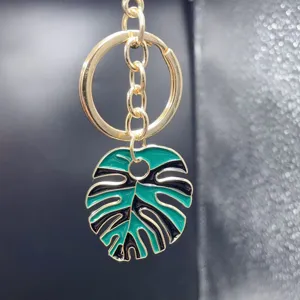 Detailed close-up of a stylish gold metal keychain featuring a green and black monstera leaf pendant.