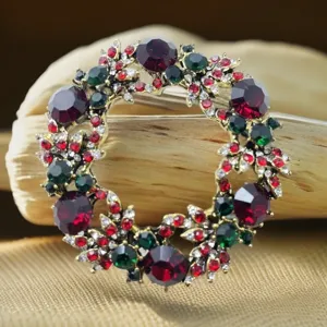 Primo piano dettaglio di spilla ghirlanda natalizia con strass rossi verdi oro.
