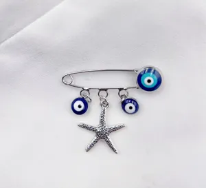 Detailed closeup of a silver safety pin brooch with blue evil eye beads and starfish charm.