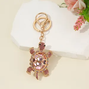 Detailed shot of sparkling pink rhinestone turtle keychain with gold hardware on white stone prop.
