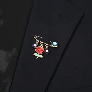 Detail view of fashion rose flower and evil eye safety pin brooch in gold tone enamel finish.