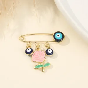 Detailed close-up of gold-tone safety pin brooch featuring blue evil eye beads and pink rose.