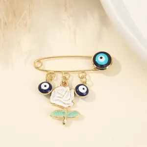 Gold-tone safety pin brooch featuring evil eye charms and a white rose pendant accessory.