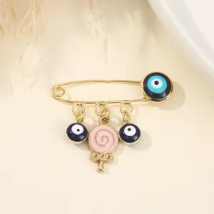 Detailed shot of a sweet gold-tone safety pin brooch featuring blue eye charms and lollipop.